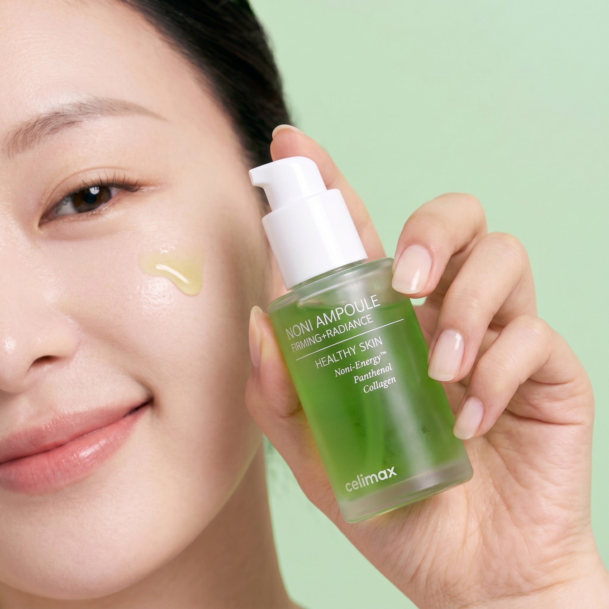 Modelo sonriente sosteniendo ampolla facial Celimax Noni de KSTANDARBEAUTY con extracto de noni, pantenol y colágeno.
