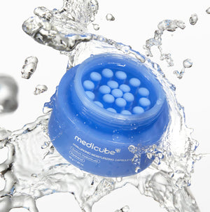 Crema hidratante KSTANDARBEAUTY Medicube con cápsulas azules de ácido hialurónico y pantenol rodeada de salpicaduras de agua